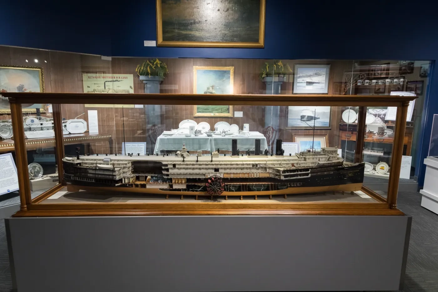 Model ship in a glass display case with paintings and artifacts in the background.