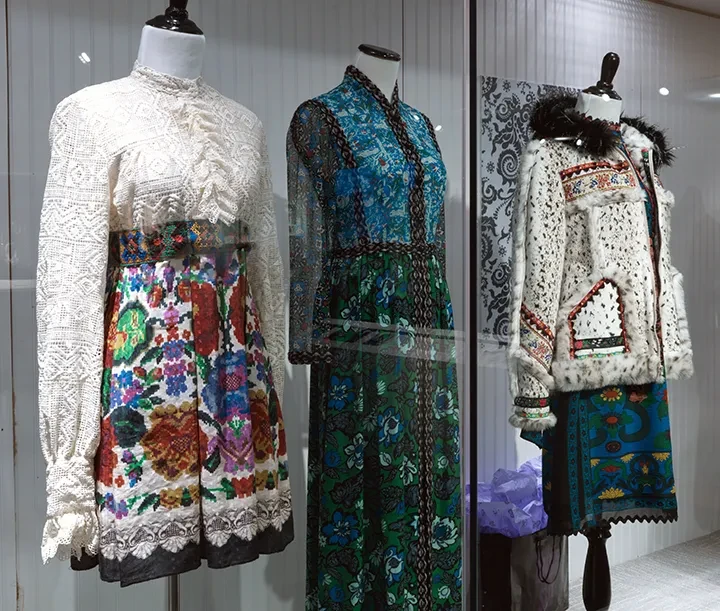 Mannequins displaying colorful, patterned dresses with lace details in a store window.
