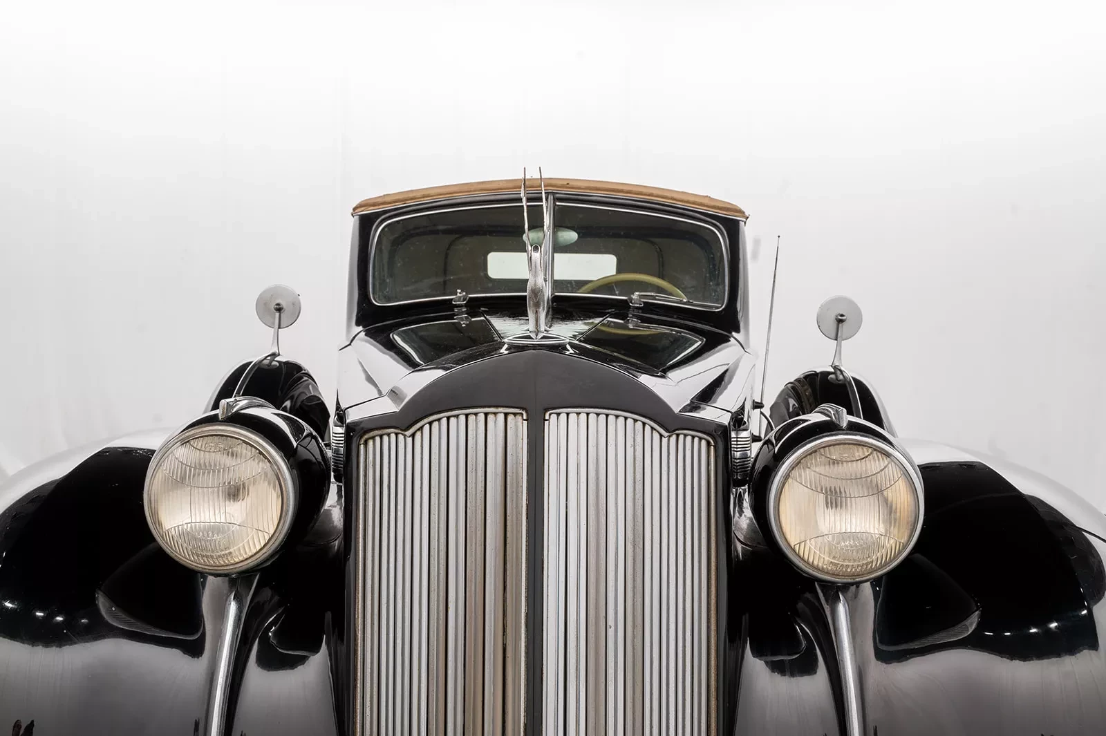 Vintage black car front, with chrome grille and round headlights on a white background.
