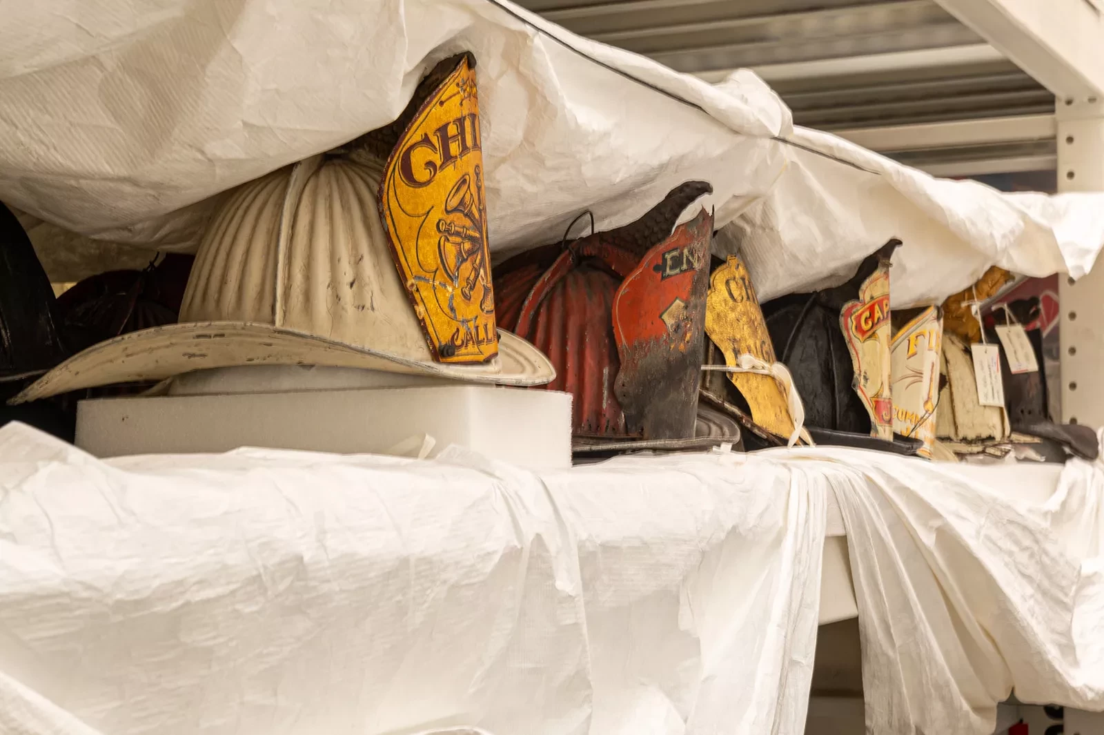 Historic firefighter helmets on a storage shelf, covered with protective wrapping.