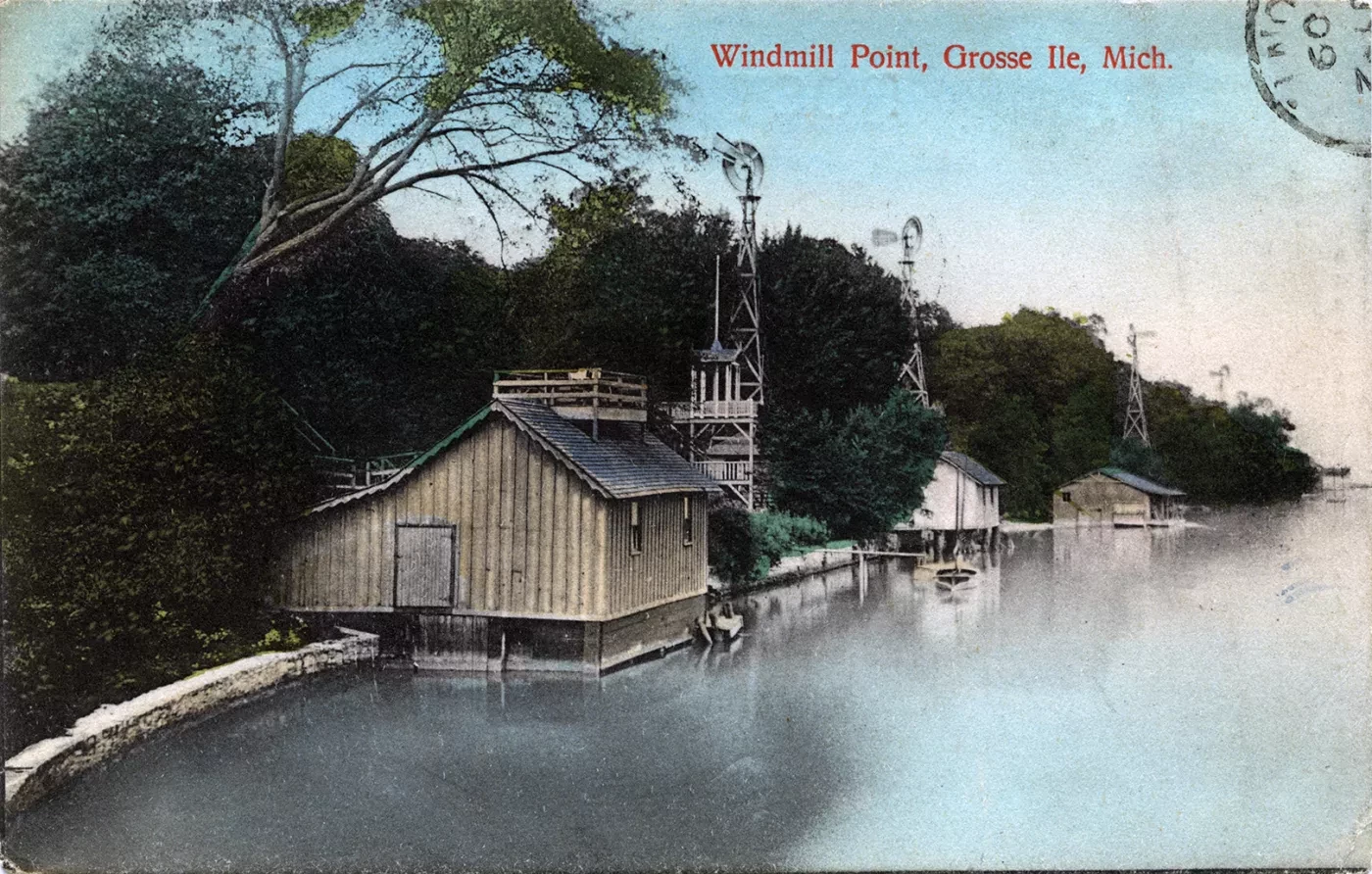 Postcard illustration of boathouses on a calm lake surrounded by trees, with windmills in the background.
