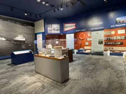 Museum exhibit room with nautical-themed displays, model ships, and historical photos on the blue and red walls.