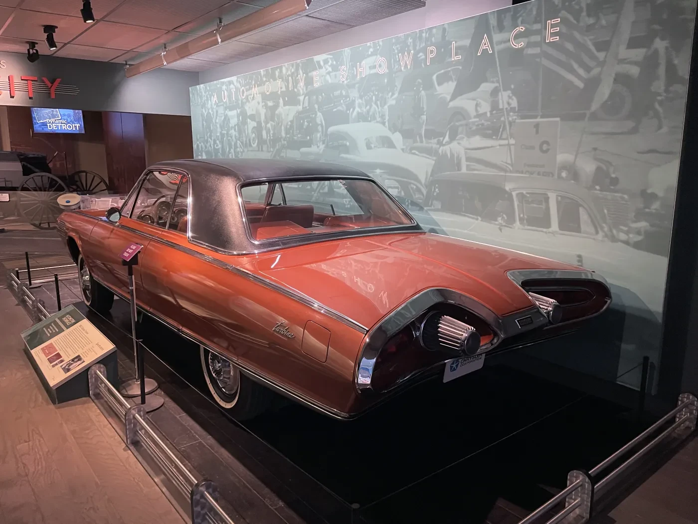 Red vintage car displayed in a museum with soft lighting and historical black-and-white photos in the background.