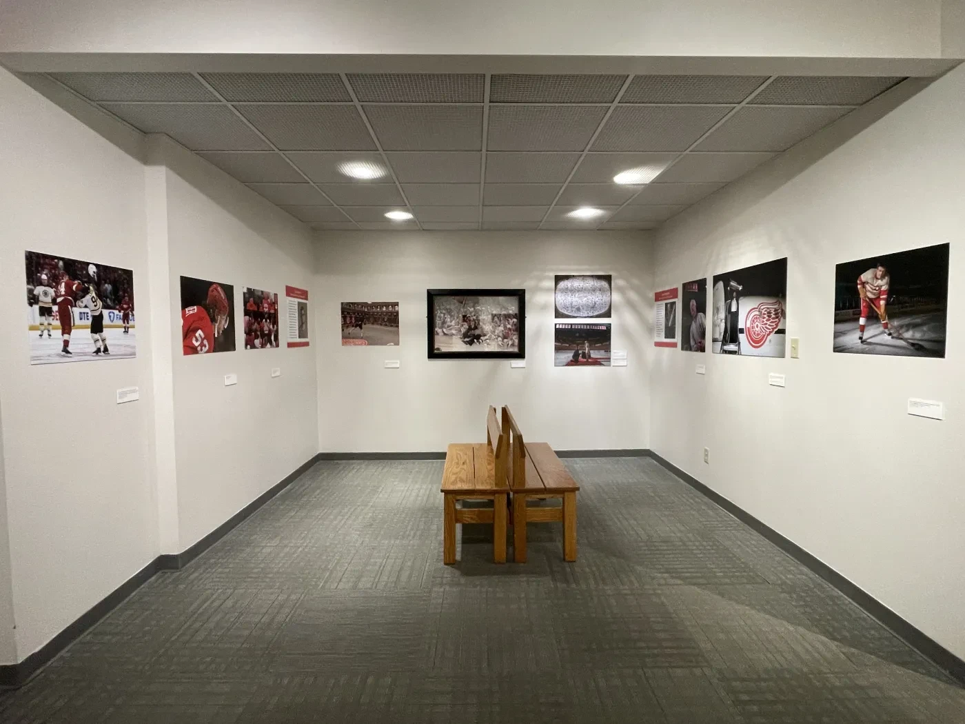 Hallway with framed sports photographs on walls, and a wooden bench in the center.