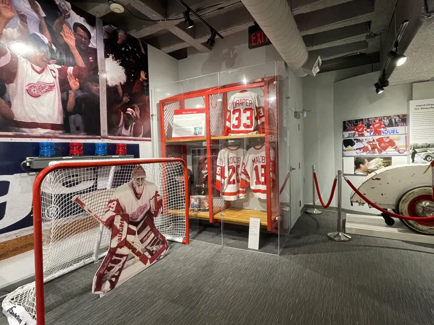 Hockey museum exhibit with jerseys, memorabilia, and a goalie cutout in front of a net.