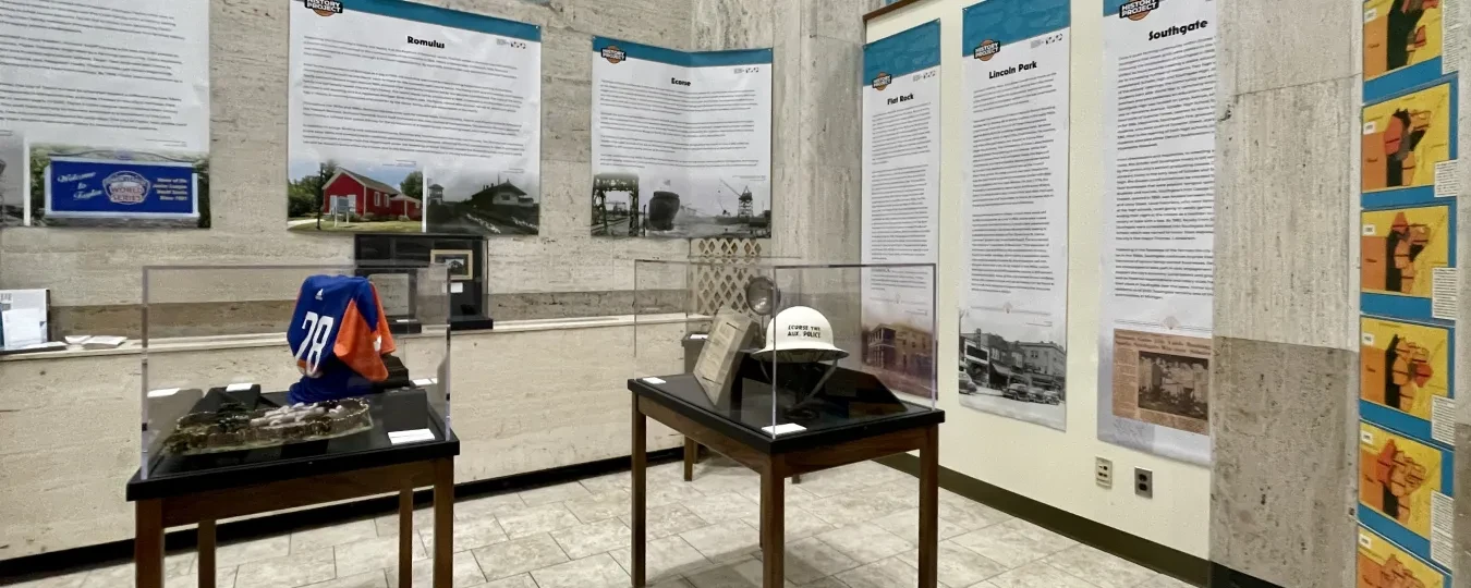 Museum exhibit with display cases and informational panels in a room with tall windows.