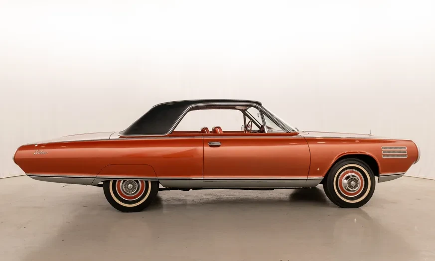 Classic orange car with a black roof in a studio setting.